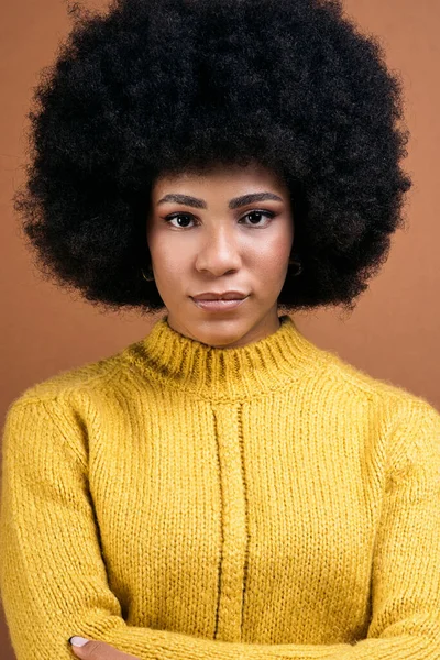 Beautiful young afro woman posing in studio shot against brown background and looking at camera.