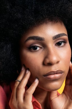 Beautiful afro woman wearing cool makeup touching her face and looking at camera in studio shot.