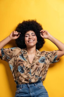 Smiley afro woman wearing colorful shirt having fun in studio shot against yellow background.