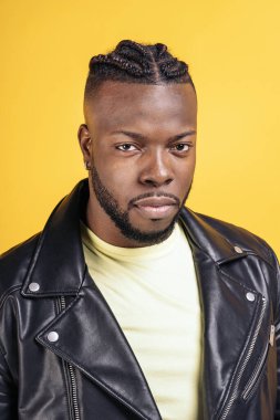 Strong black man wearing black leather jacket posing in studio shot against yellow background.
