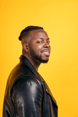 Confident black man wearing black leather jacket smiling and looking at camera in studio shot.