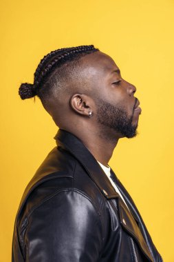 African american man with cool hairstyle and wearing black leather jacket posing in studio shot against yellow background.