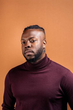Black man with expressive eyes looking at camera in studio shot against brown background.