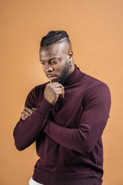 Black man with expressive eyes looking down in studio shot against brown background.