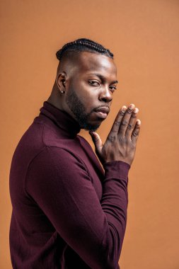 Black man with expressive eyes looking at camera in studio shot against brown background.