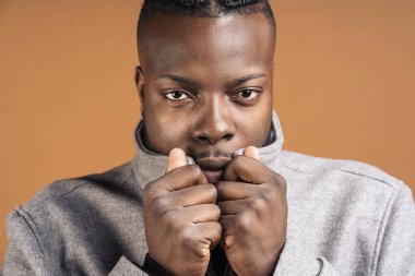 Black man with expressive eyes looking at camera in studio shot against brown background.