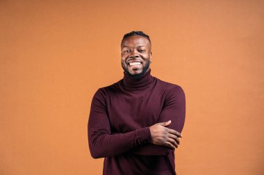Cheerful black man wearing black leather jacket smiling in studio shot and looking at camera against brown background.