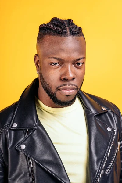 Strong black man wearing black leather jacket posing in studio shot against yellow background.