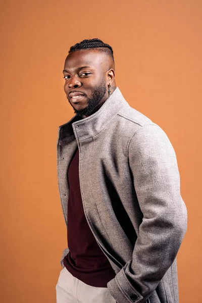 Strong black man wearing elegant clothes posing in studio shot against brown background.