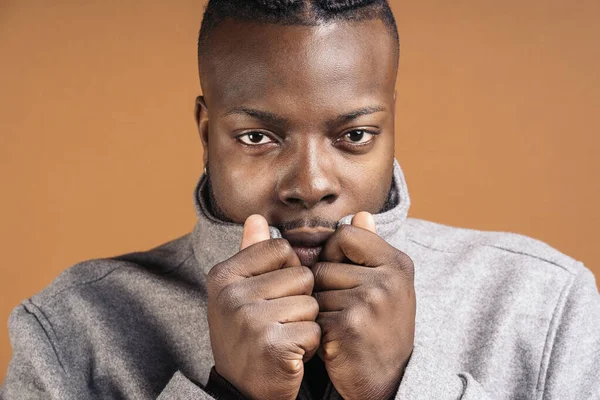 Black man with expressive eyes looking at camera in studio shot against brown background.