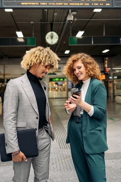 Business african man with curly hair talking with his female colleague and using mobile phone. They are in Atocha train station in Madrid.