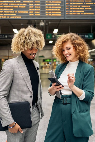 Business african man with curly hair talking with his female colleague and using mobile phone. They are in Atocha train station in Madrid.