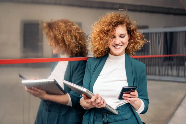 Happy business woman with curly hair and beautiful suit using her mobile phone outdoors.