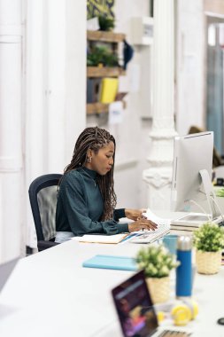 Focused black woman with braids sitting in her desk in the office and working with her laptop.