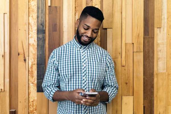 Young black business man using his mobile phone and standing against wooden background.