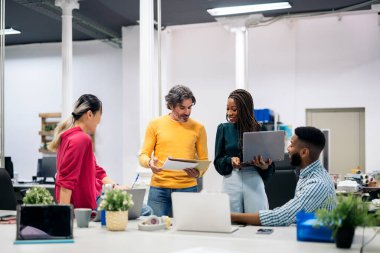 Multicultural teamwork talking and using laptops in a modern bright office. Co-working concept