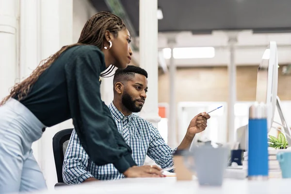 Focused black business woman working in the office with her colleague and using laptop.