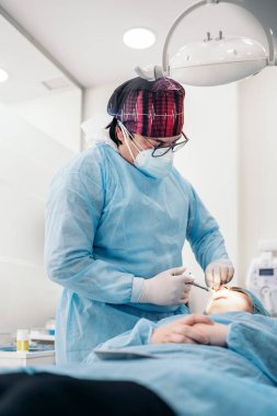 Dentist man wearing face mask and protective clothes putting injection to unrecognized patient.