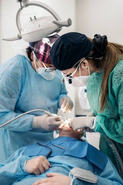 Dentist wearing face mask and dental magnifying glasses doing treatment to unrecognized patient.