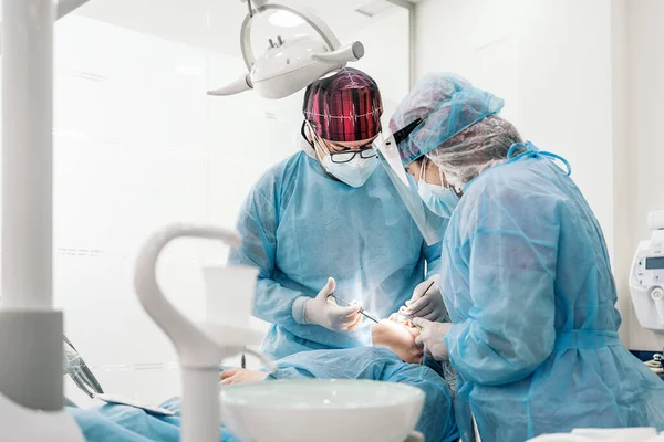 Male dentist and his team wearing face mask and protective clothes putting dental injection to unrecognized patient