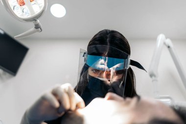 Young female dentist wearing face mask and dental magnifying glasses during surgery.