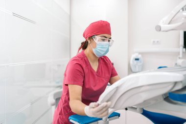 Female dentist working in modern dental clinic and wearing face mask. She is also wearing dental safety glasses.