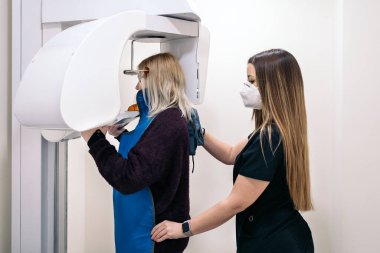 Female dentist helping unrecognized patient to use x- ray machine used in dental clinic.