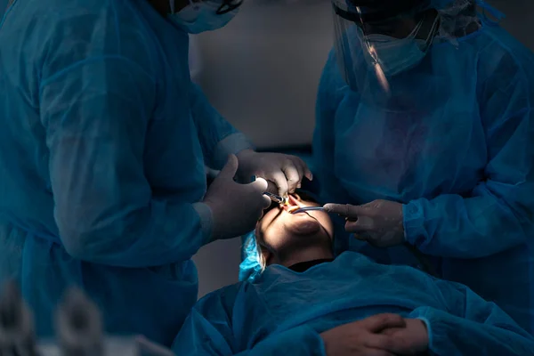 Dentist team wearing face masks and hair nets working in dental clinic with adult patient.