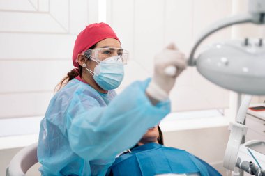 Dentist wearing face mask and hair net working in dental clinic with unrecognized patient.
