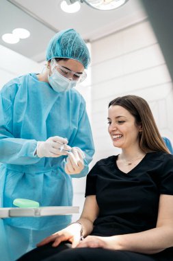Dentist wearing face mask and special protective clothes explaining to her patient how to use teeth covers.
