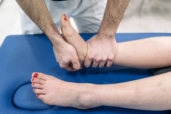 Male physiotherapist giving feet massage to unrecognized woman lying in stretcher.