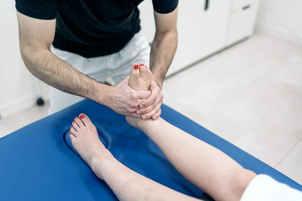 Male physiotherapist giving feet massage to unrecognized woman lying in stretcher.