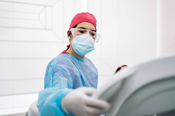Female dentist wearing protective face mask and hair net using equipment.