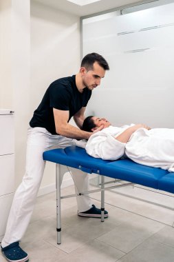 Male physiotherapist giving neck massage to relaxed woman lying in stretcher.