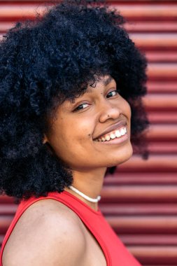 Afro saçlı güzel siyah kadın gülümsüyor ve kırmızı arka planda kameraya bakıyor..