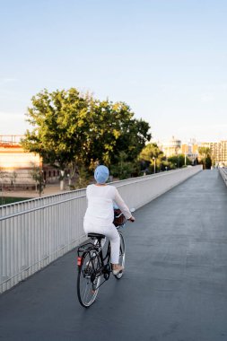 Güneşli bir günde yaya köprüsünde bisiklet süren Müslüman bir kadının dikey görüntüsü..
