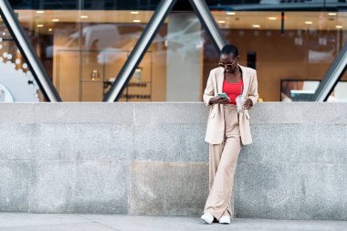 Kısa saçlı, güneş gözlüklü, beton korkuluklara yaslanmış zarif yetişkin bir kadının tam önü. Ya da şehirdeki küçük bir duvarın üzerinde telefon kullanarak ve smoothie tutarak.