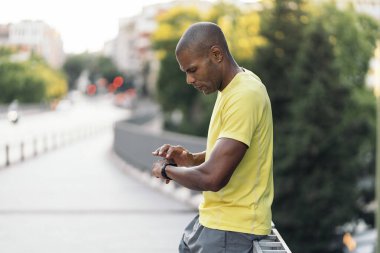 Sarı tişörtlü Afro-Amerikan bir adamın şehirde spor yapmak için akıllı gözlük kullanmasının yan görüntüsü..
