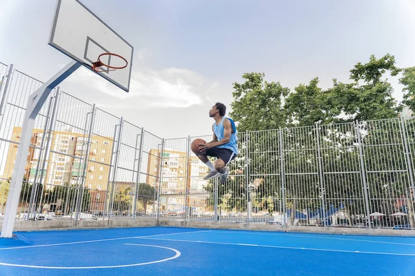 Unrecognized african boy wearing sports clothes playing basketball and throwing the ball.