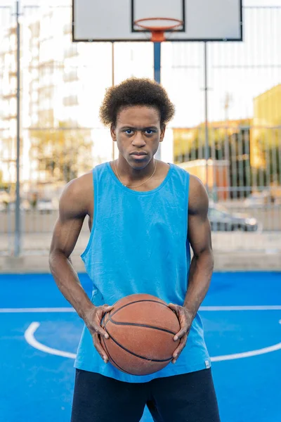 ストリートバスケットボールコートで手でボールを保持するカメラを見て集中アフロアメリカのバスケットボール選手 — ストック写真