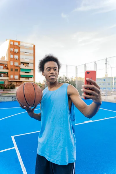 若いですアフリカ系アメリカ人バスケットボール選手取りますAセルフィー保持ザボールでストリートバスケットボールコート — ストック写真
