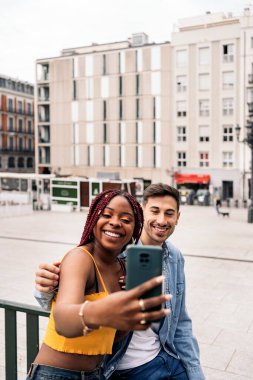 Mutlu genç arkadaşlar sokakta telefonlarıyla selfie çekiyor ve eğleniyorlar..