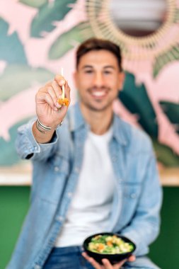 Tanınmayan mutlu adam restoranda oturmuş sağlıklı bir kasenin tadını çıkarıyor ve çubuk kullanıyor..