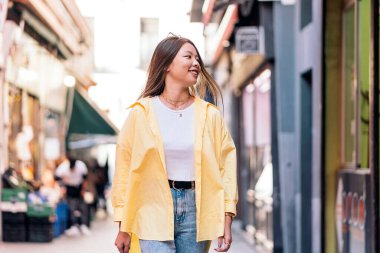 Sıradan kıyafetler giyen modaya uyan Asyalı kadın gülümsüyor ve sokağa bakıyor..