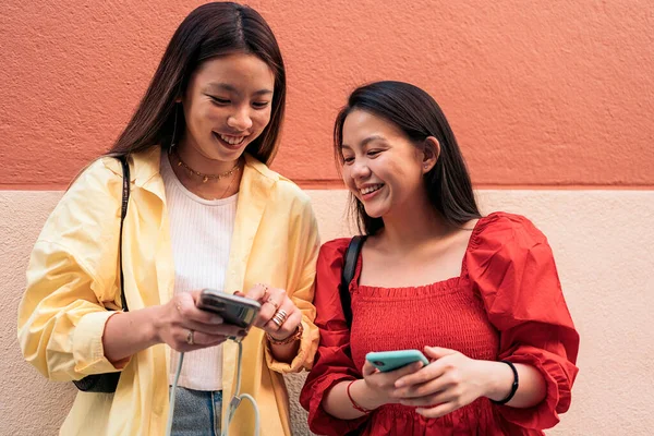 若いかなりアジア系の女性の友人が路上で彼らの携帯電話を笑って使用して — ストック写真