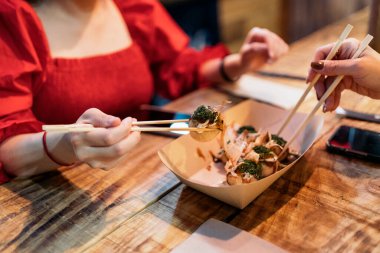 Tanınmayan genç bir kadın arkadaşıyla Çin restoranında yemek yiyor ve çubuk kullanıyor..