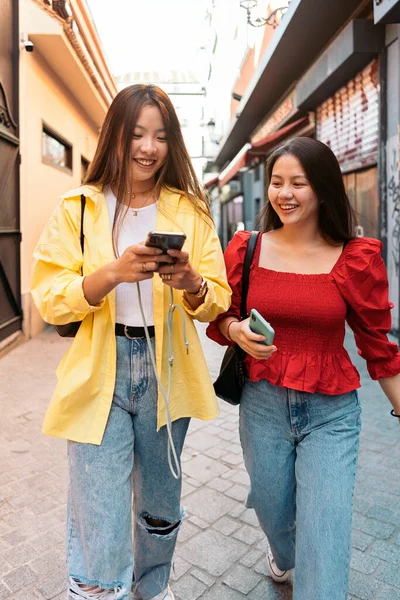 若いとかなりアジアの女性の友人が話して 路上で自分の携帯電話を使用して — ストック写真