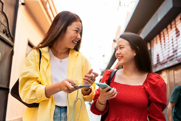Young and pretty asian female friends talking and using their phones in the street.