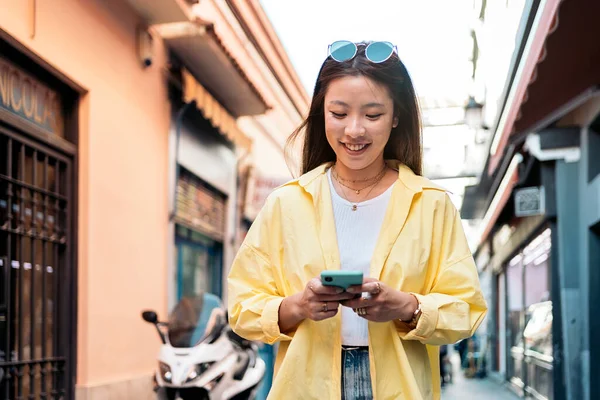流行の服を着たクールなアジアの女性が街を歩き 彼女のスマートフォンを使用しています — ストック写真