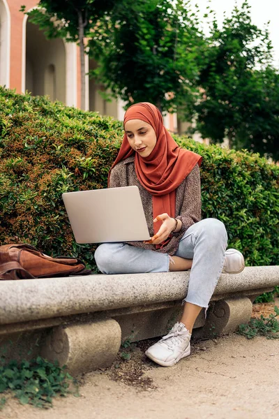 若いイスラム教徒の女性ヒジャーブを着て公園に座って 彼女のコンピュータを使用して — ストック写真